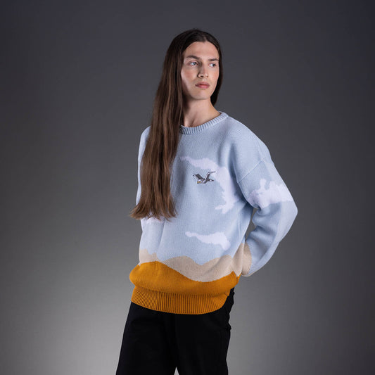 Side view of a light-blue knitted unisex crewneck featuring all-over cloud patterns and a bird motif on the right-hand side chest. The hem and sleeve cuffs are finished with a mustard-coloured edge.