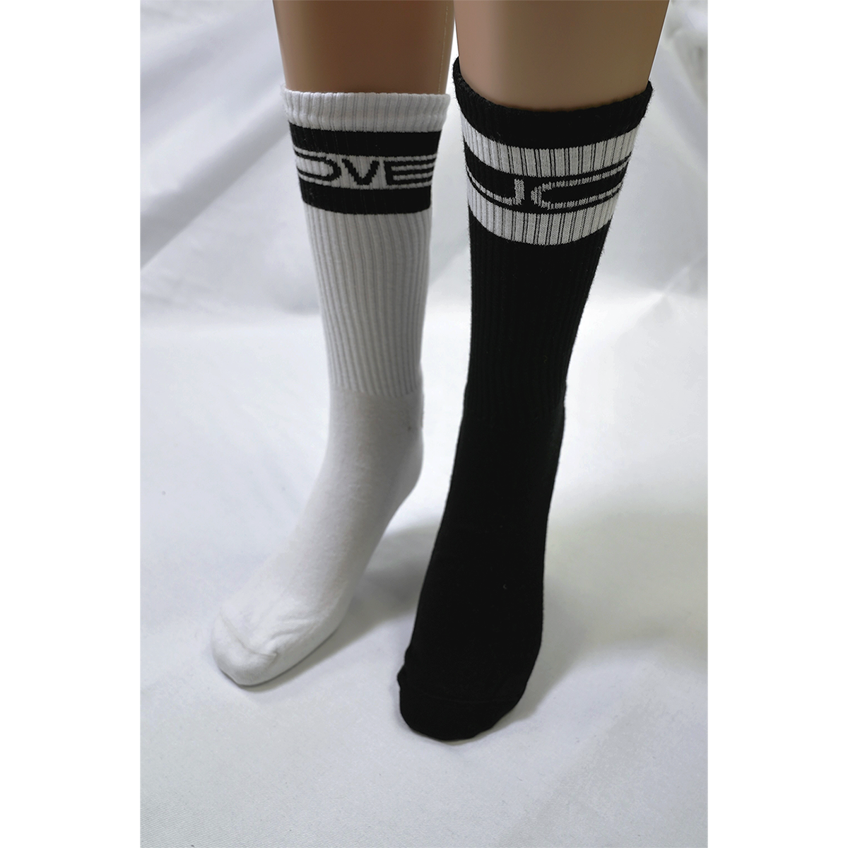 Front view of legs and feet wearing long socks: the right foot has a white sock with black “Lovejoy” text at the top, and the left foot wears a black sock with white “Lovejoy” text at the top.