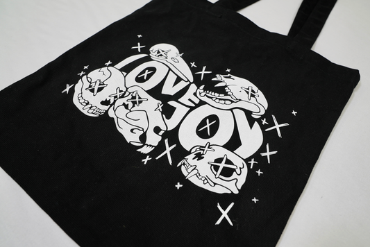 Focused front view of a black tote bag featuring a centred white “Lovejoy” text print surrounded by skull graphics.