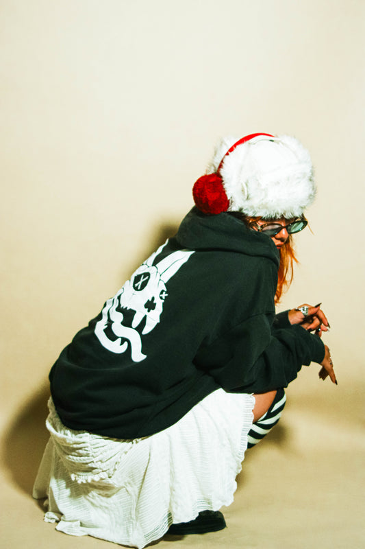 Woman sat down wearing an oversized unisex hoodie with a white Lovejoy skull cat print across the back.