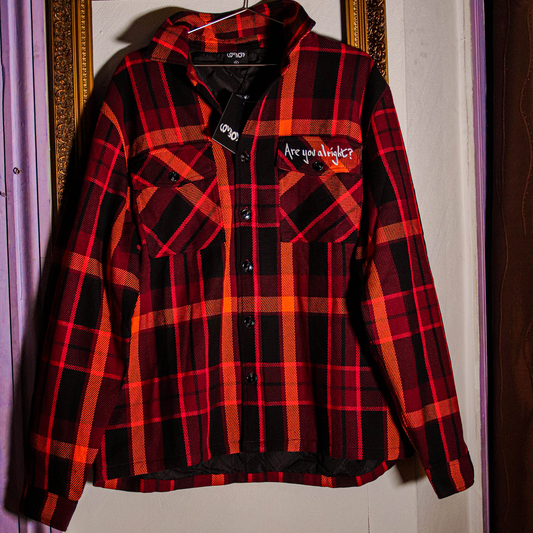 Front image of a red quilted shirt featuring a collar, button-up front, and a chest pocket on the right-hand side with white embroidered text that reads “Are you alright.