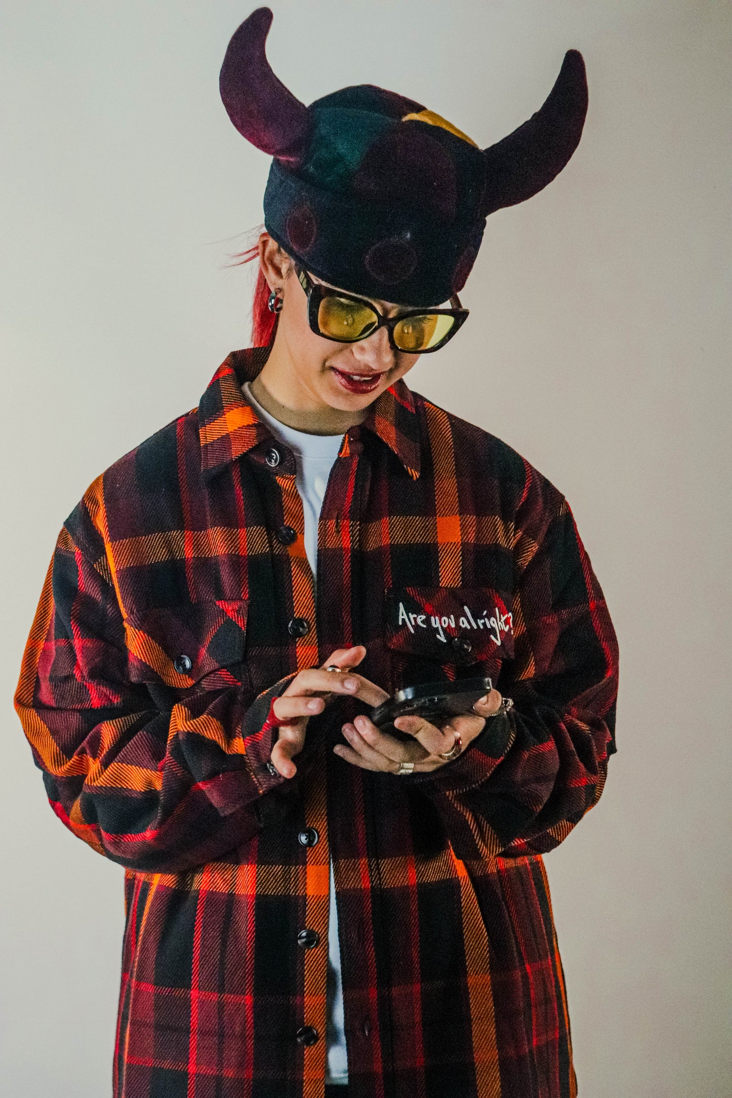 Front image of a red quilted shirt featuring a collar, button-up front, and a chest pocket on the right-hand side with white embroidered text that reads “Are you alright.