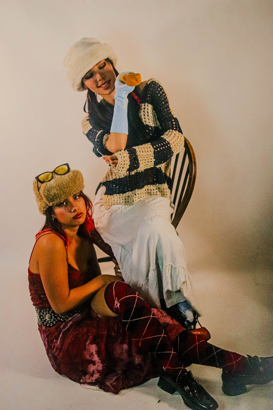 Image of two people in a room - one seated on a chair, the other sitting on the floor wearing red knee-high tartan socks.